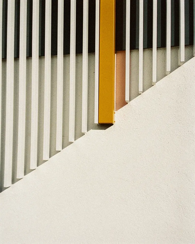 A row of narrow off-white fins casting hard parallel shadows, one fin painted amber.