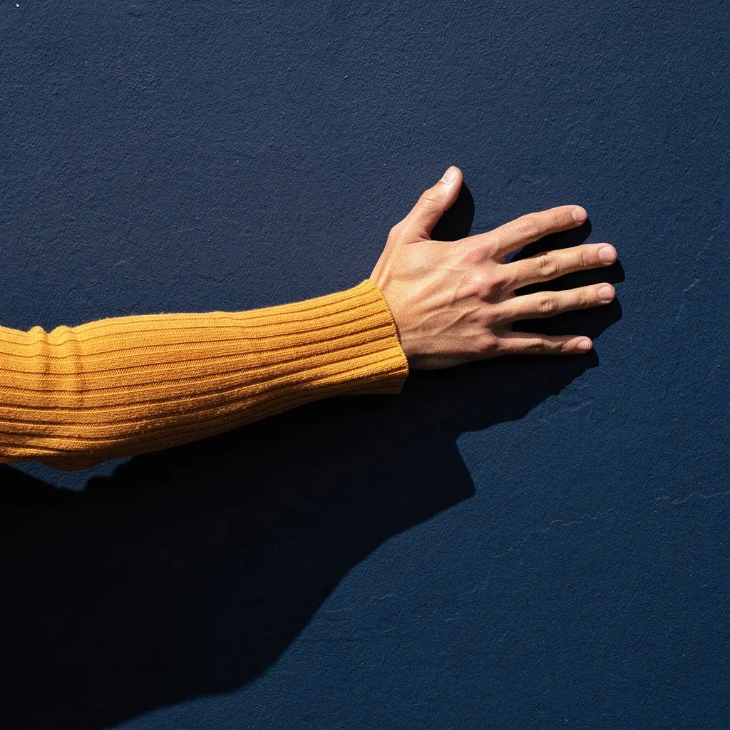 An arm in an amber ribbed sleeve pressed flat against a deep navy wall in hard sunlight.